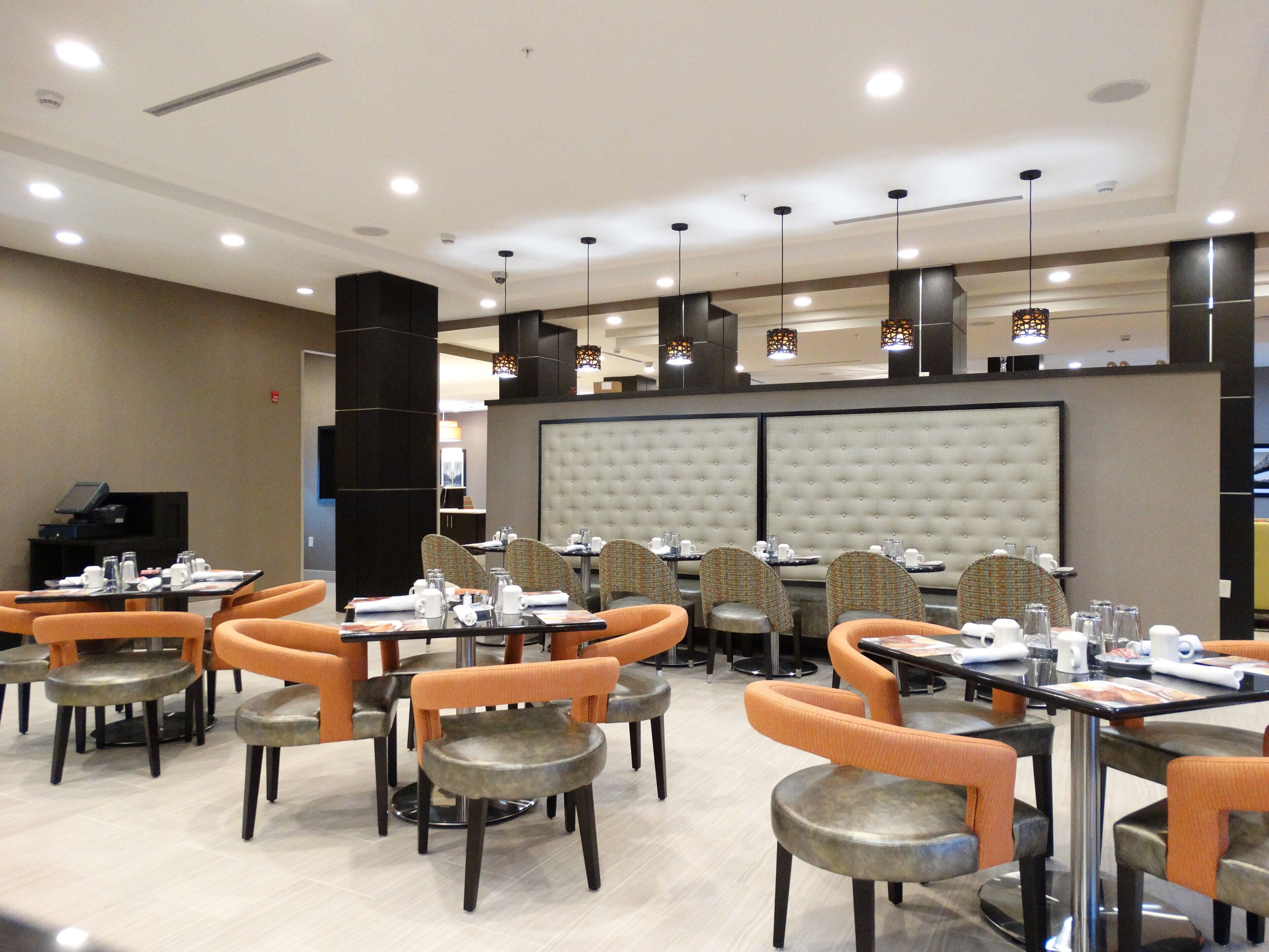 A dining area with multiple tables and chairs, a large cushioned partition wall, and pendant lighting.