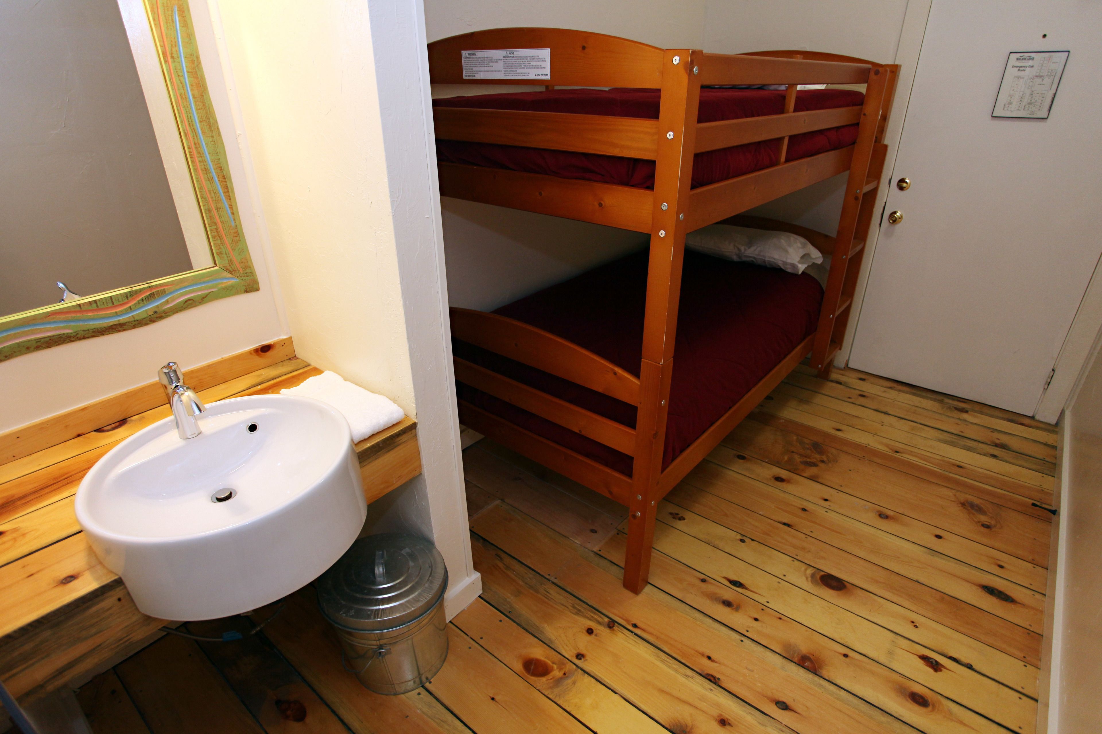 A bunk bed with a wooden headboard, a white sink with a mirror, and a wooden floor.