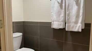 Un baño con inodoro, paredes de azulejos oscuros y dos toallas blancas colgadas de un perchero.