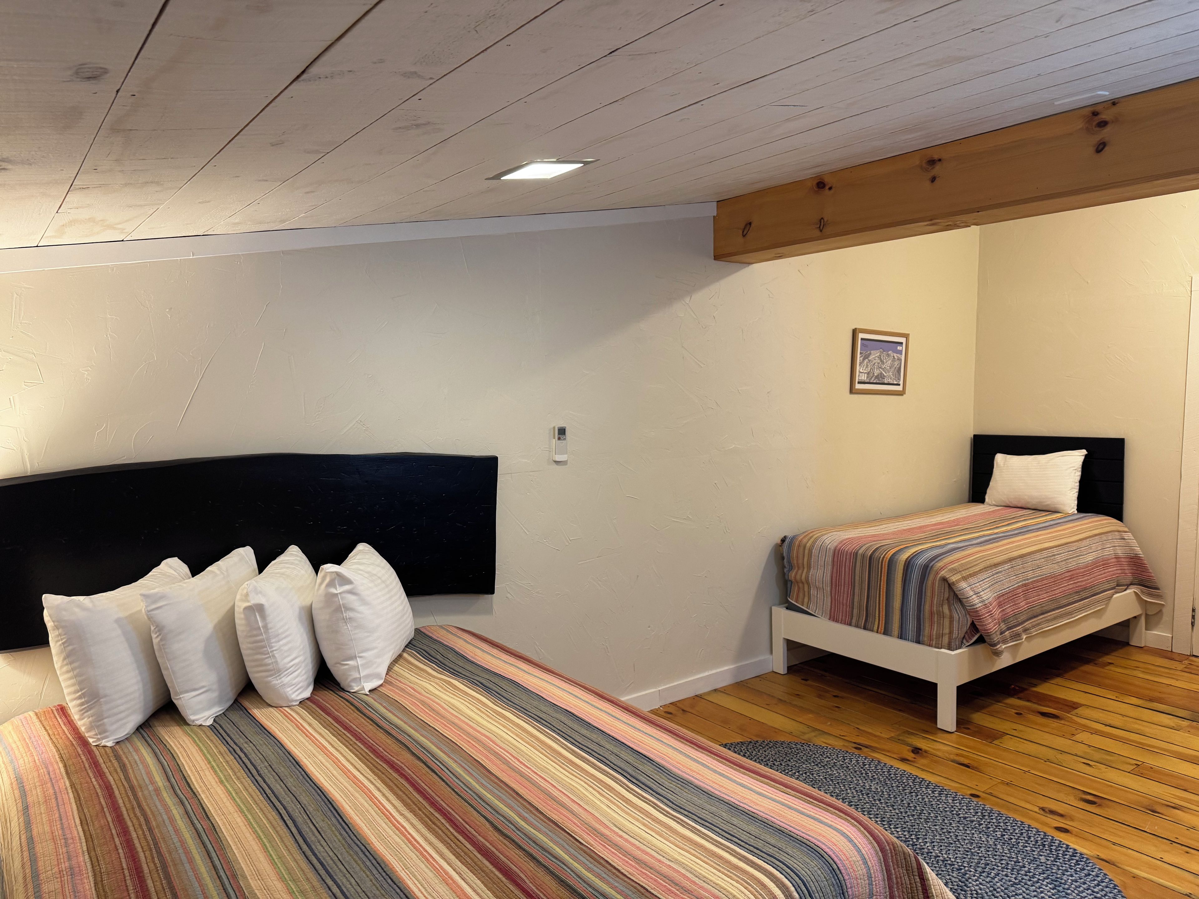 Un dormitorio con dos camas, piso de madera y techo con vigas a la vista.