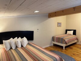 Un dormitorio con dos camas, piso de madera y techo con vigas a la vista.