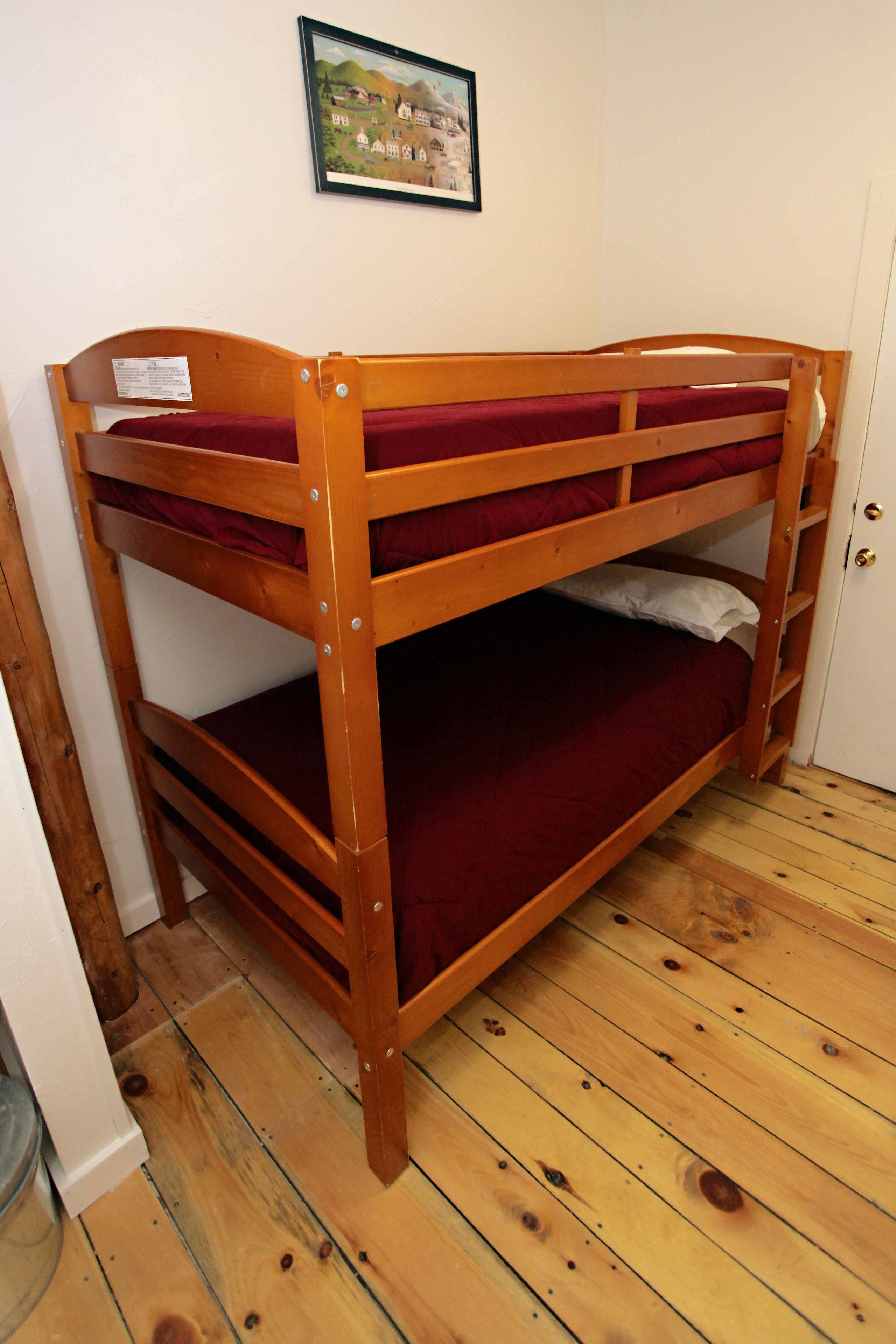Uma cama beliche com colchão vermelho em um quarto com piso de madeira e porta branca.