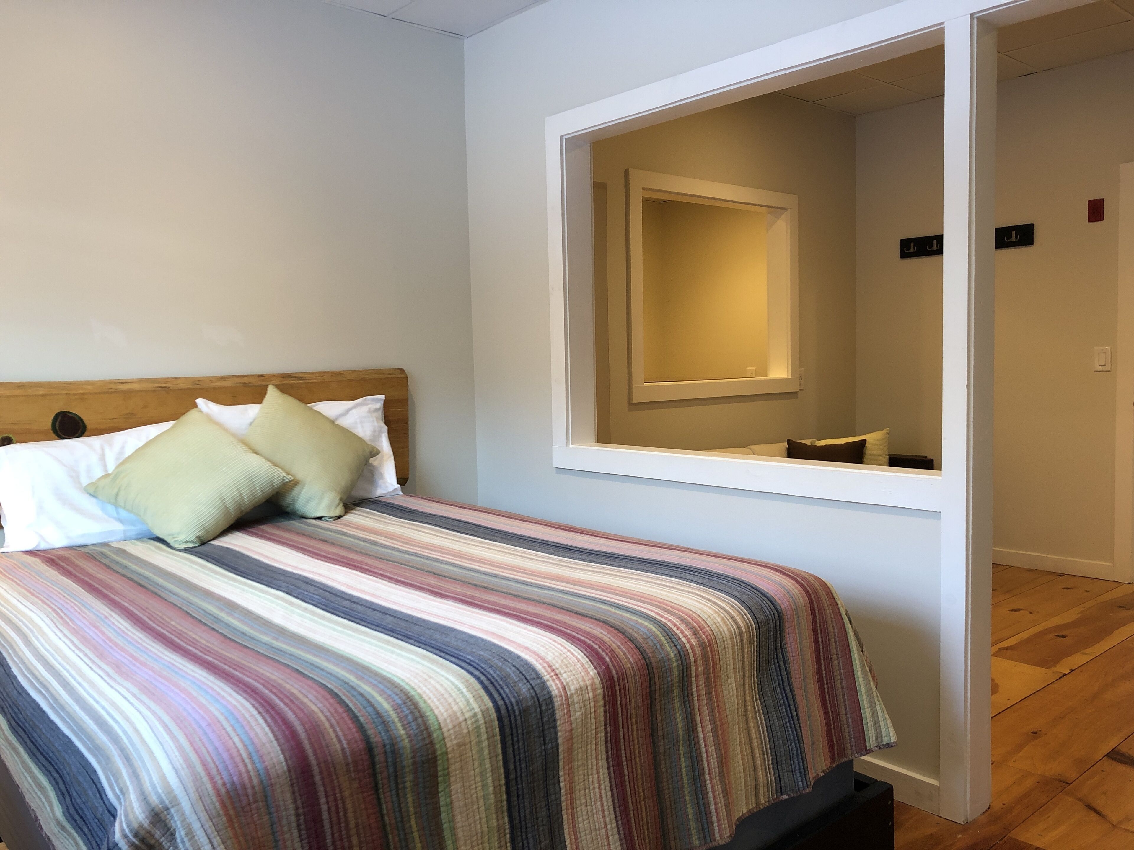 Un lit bien fait, avec une couvre-lit à rayures, une tête de lit en bois et deux oreillers. Un grand miroir est accroché au mur, au-dessus du lit.