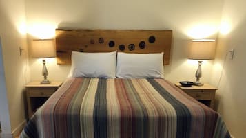 Una cama con colcha a rayas, dos almohadas blancas y un cabecero de madera con adornos circulares. Hay dos mesitas de noche con lámparas a cada lado de la cama.