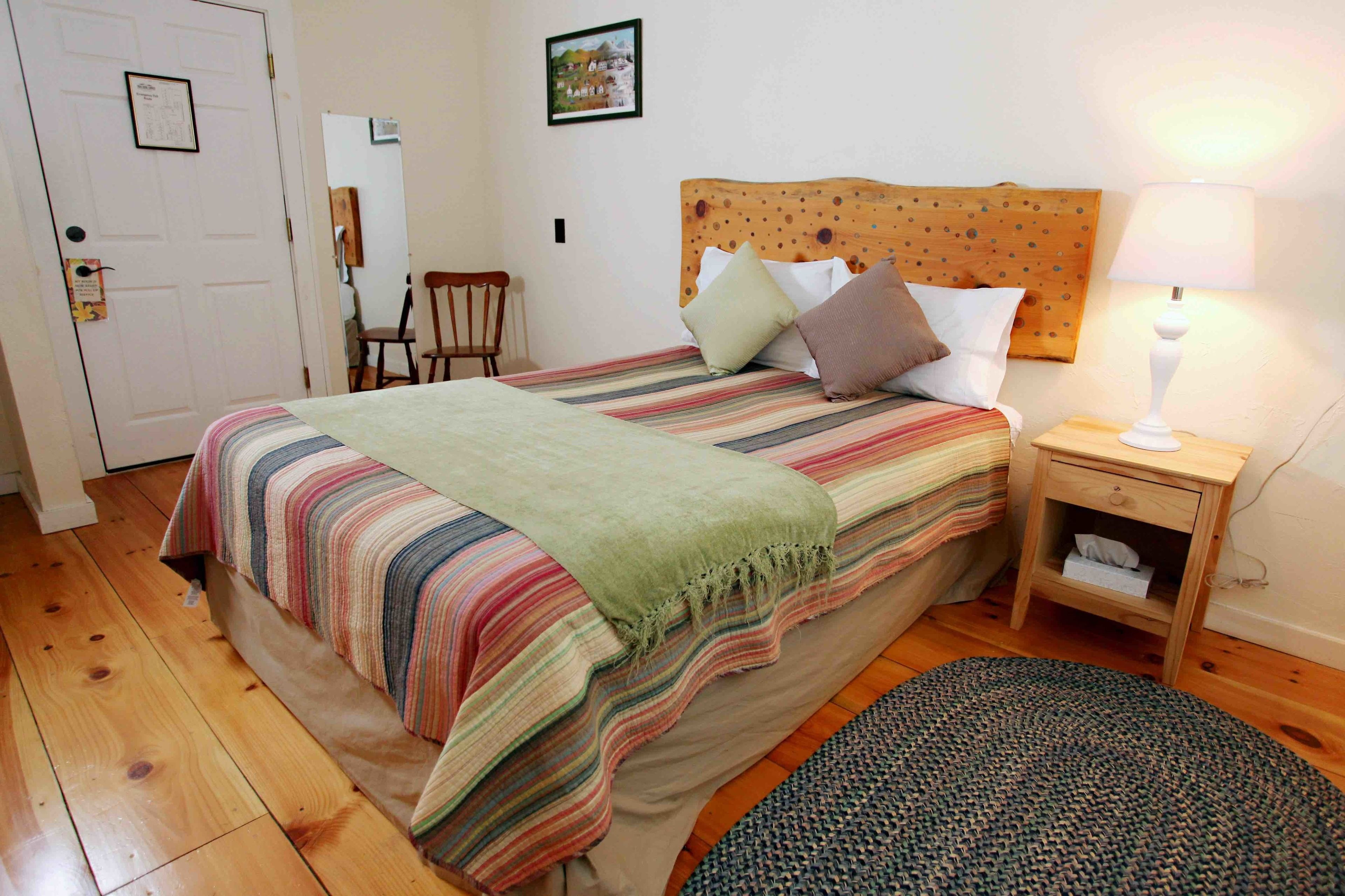 Quarto com cama, mesa de cabeceira, cadeira e porta.