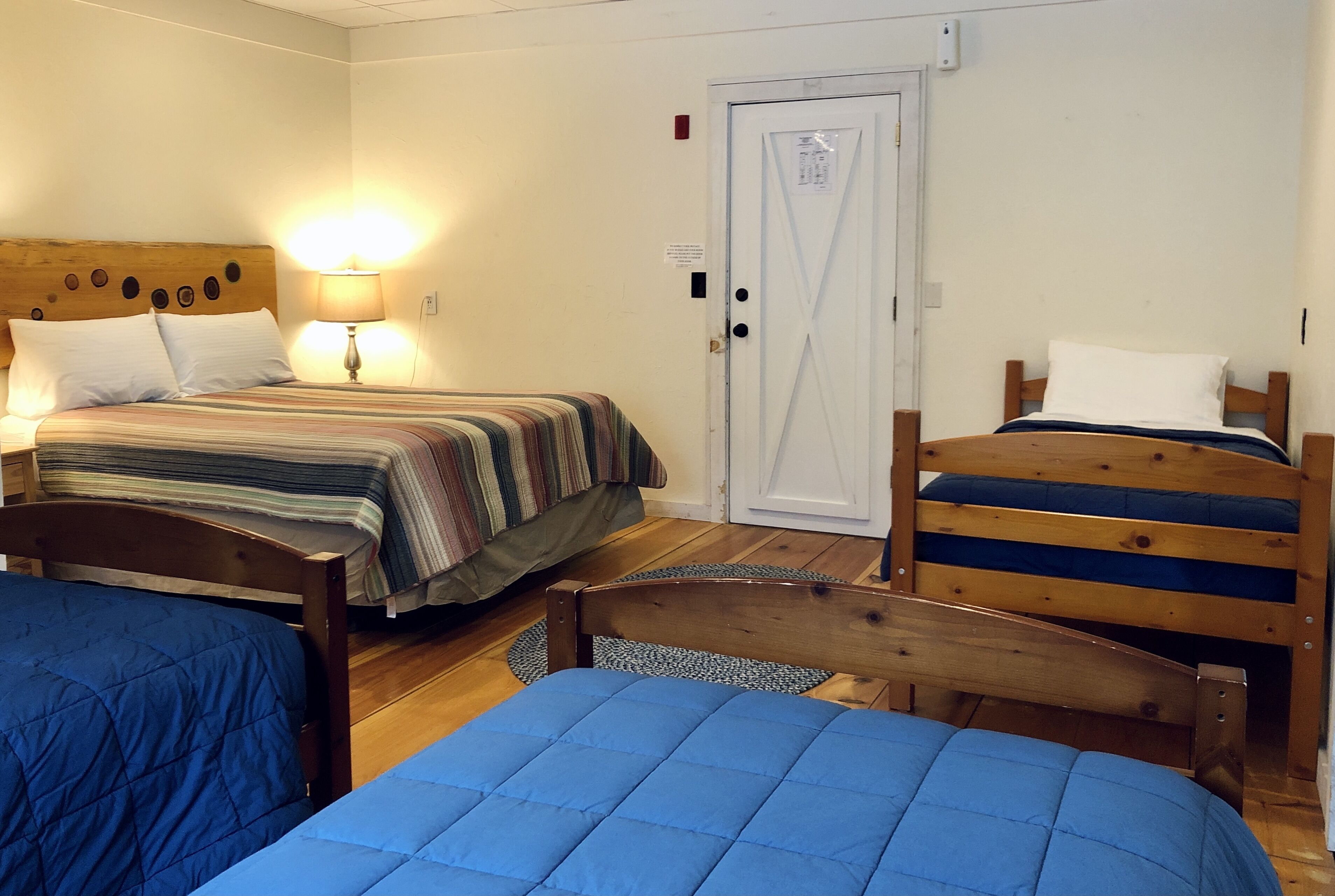 A room with two beds, a wooden headboard, a lamp, and a door.