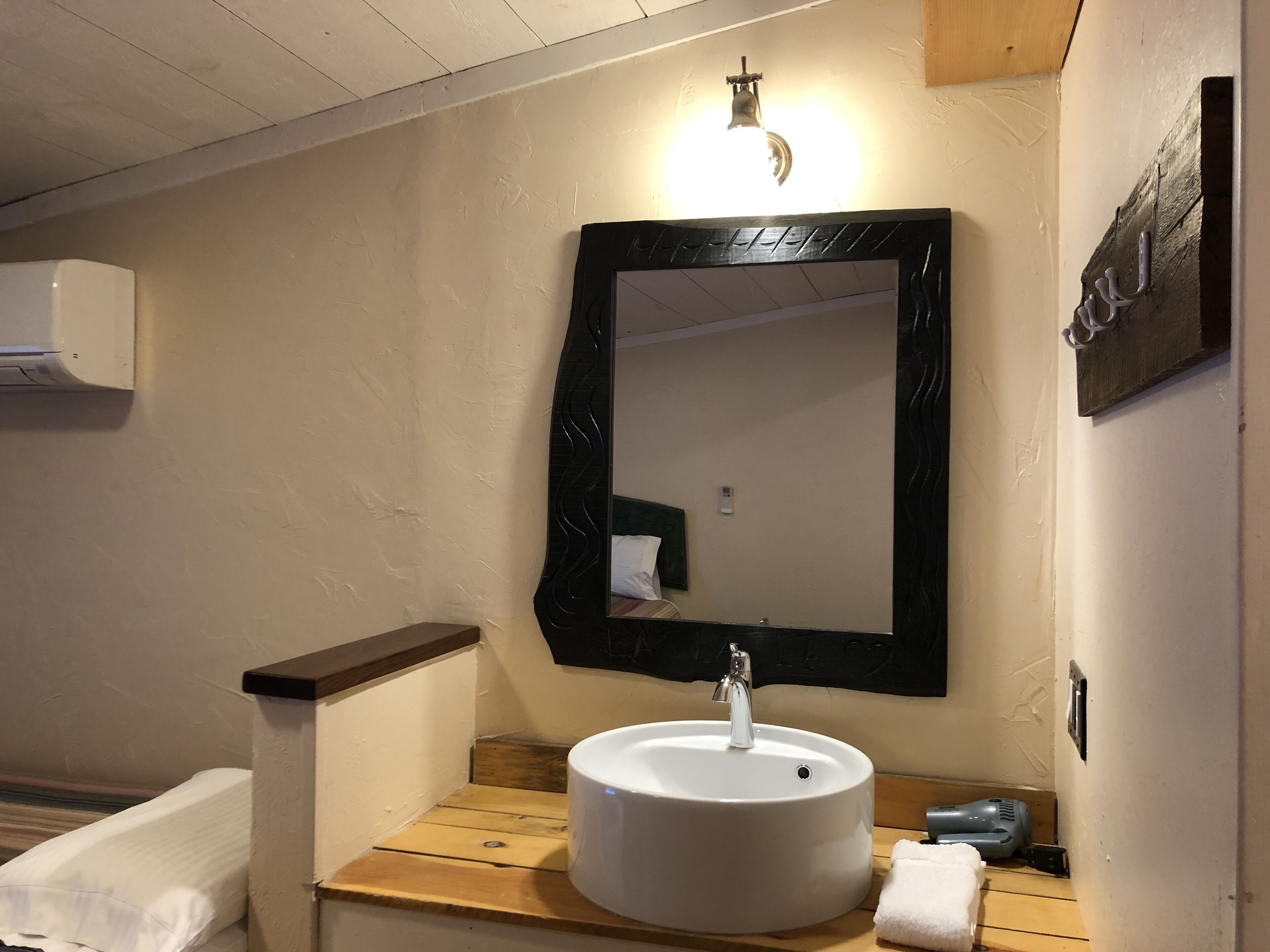 Un baño con un lavamanos blanco, un tocador de madera, un espejo con marco negro y una toalla sobre la encimera.