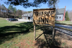 Un letrero de madera anuncia Trailside Inn, mostrando una vista despejada de los alrededores, incluyendo coches estacionados y un edificio al fondo.