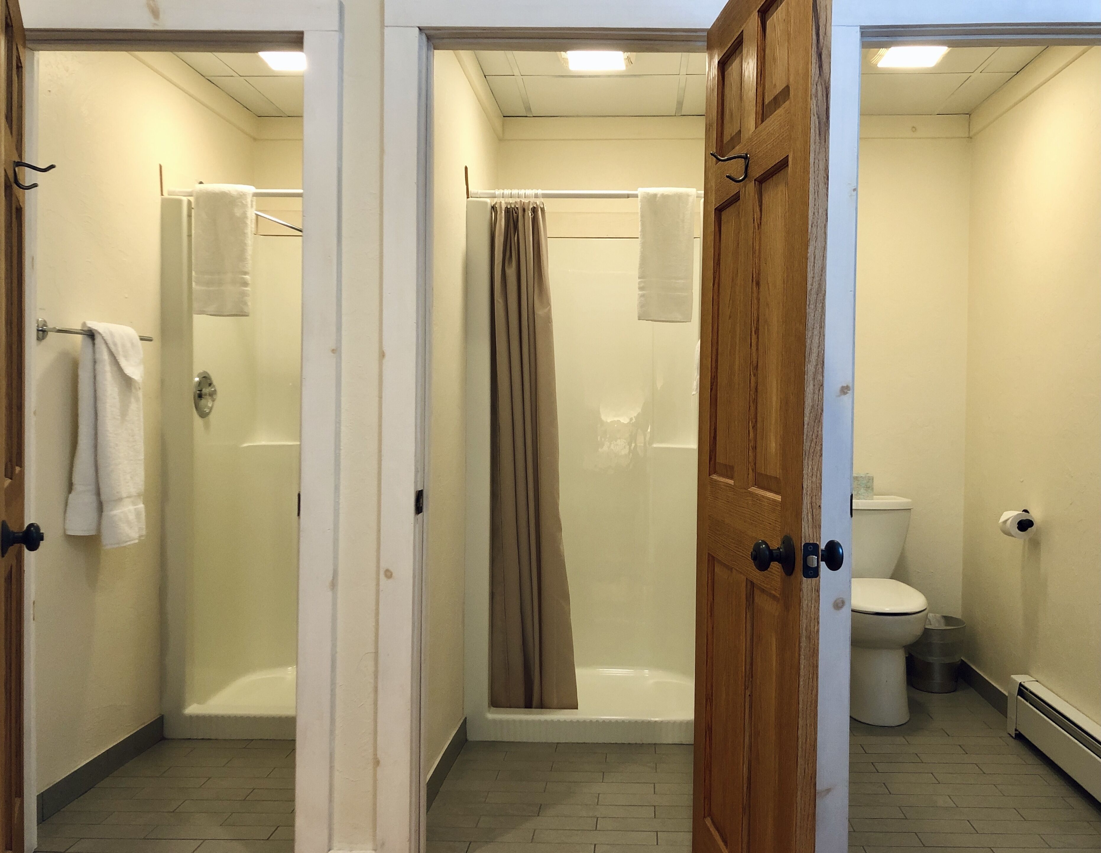 A bathroom with a shower, toilet, and a door leading to another room.