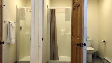 A bathroom with a shower, toilet, and a door leading to another room.