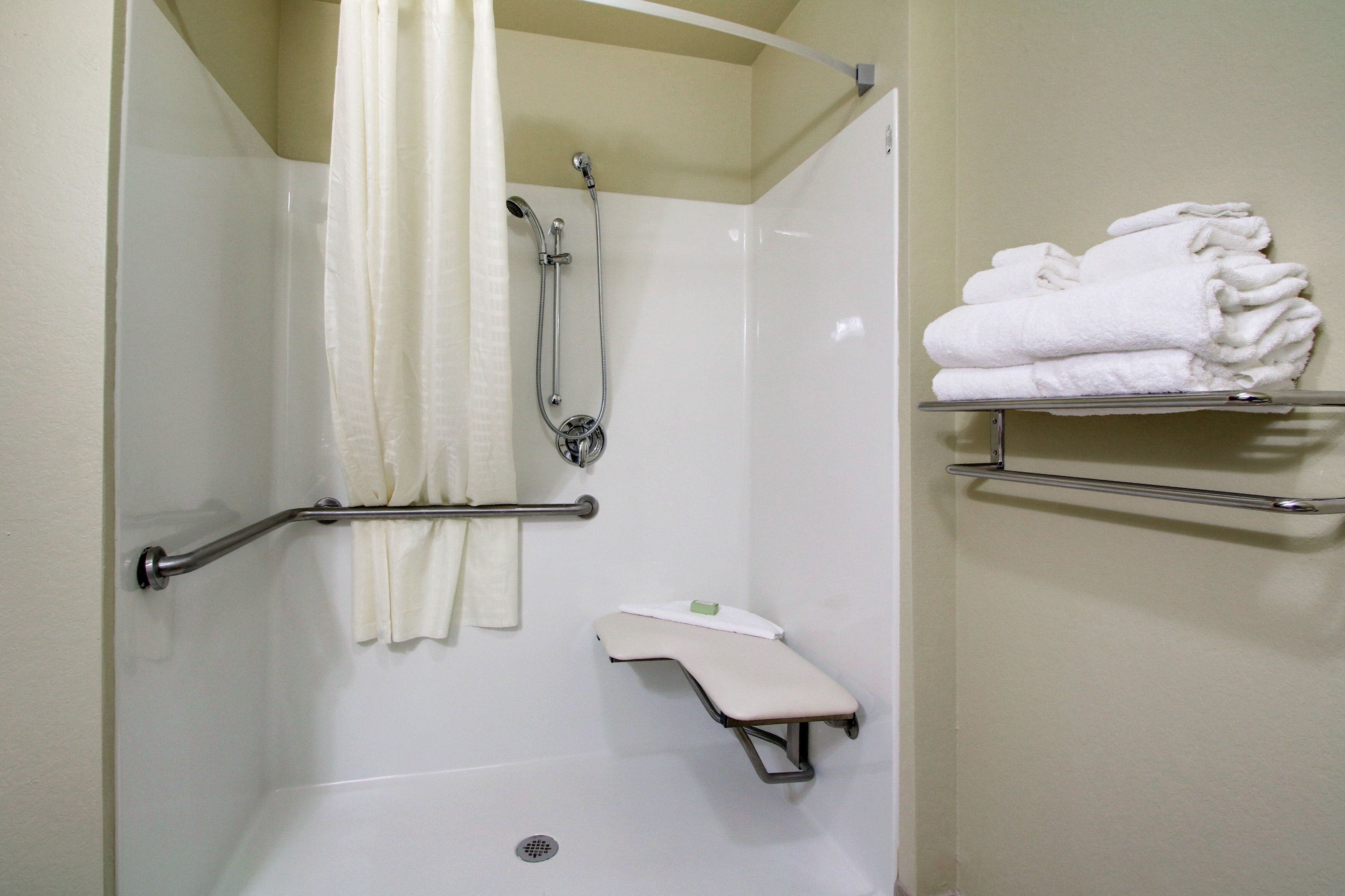 A shower area with a grab bar, a shelf with folded towels, and a small shelf with a soap dish.