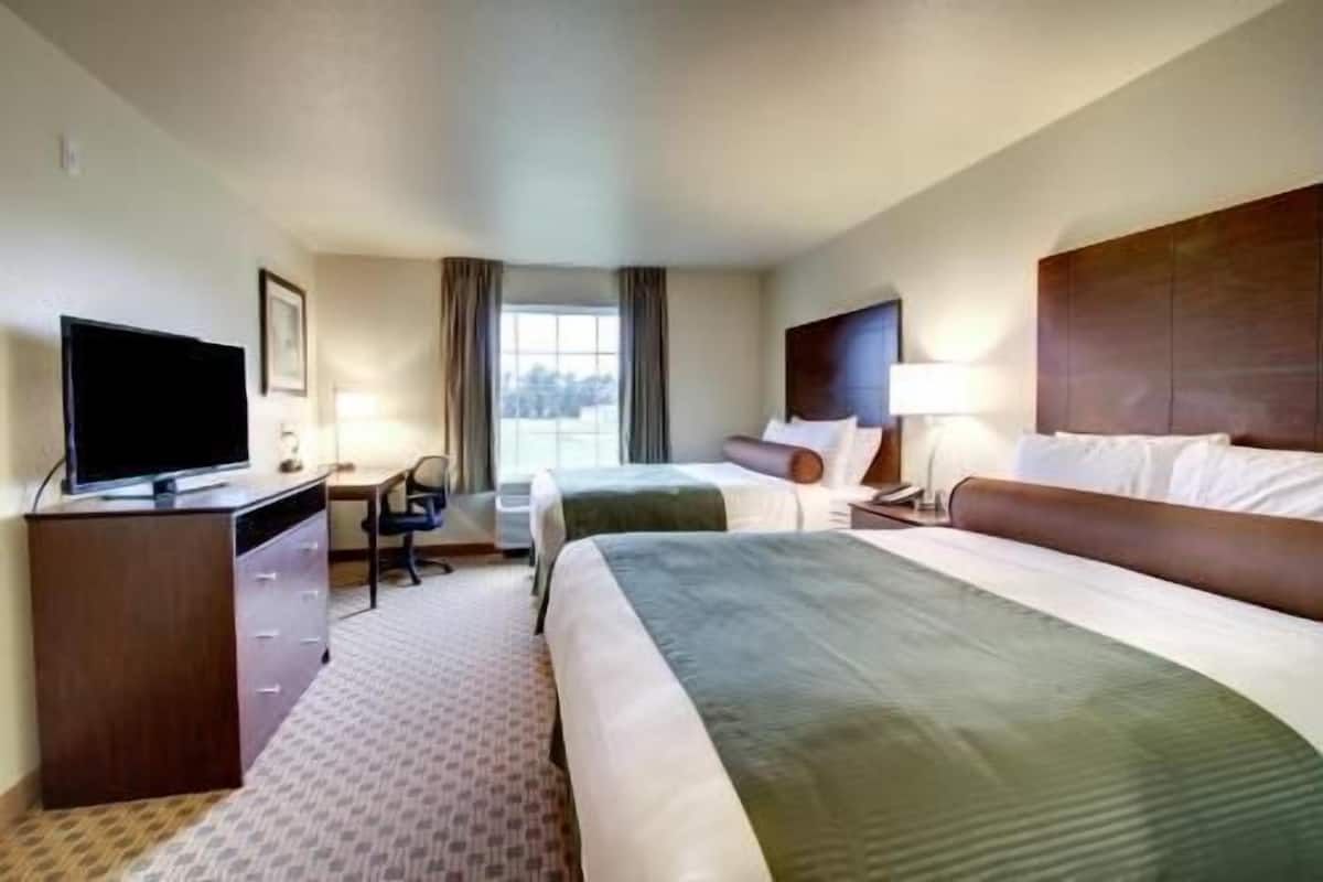 A hotel room with a bed, a desk with a TV, a chair, and a window.