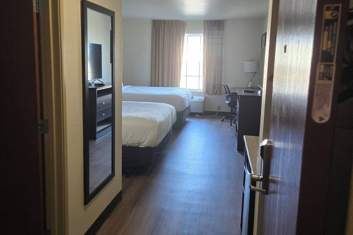 A hotel room with a bed, a desk, a chair, a mirror, and a window with curtains.