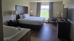 A hotel room with a large bed, a desk, a TV, a bathroom with a sink and bathtub, and a window with curtains.