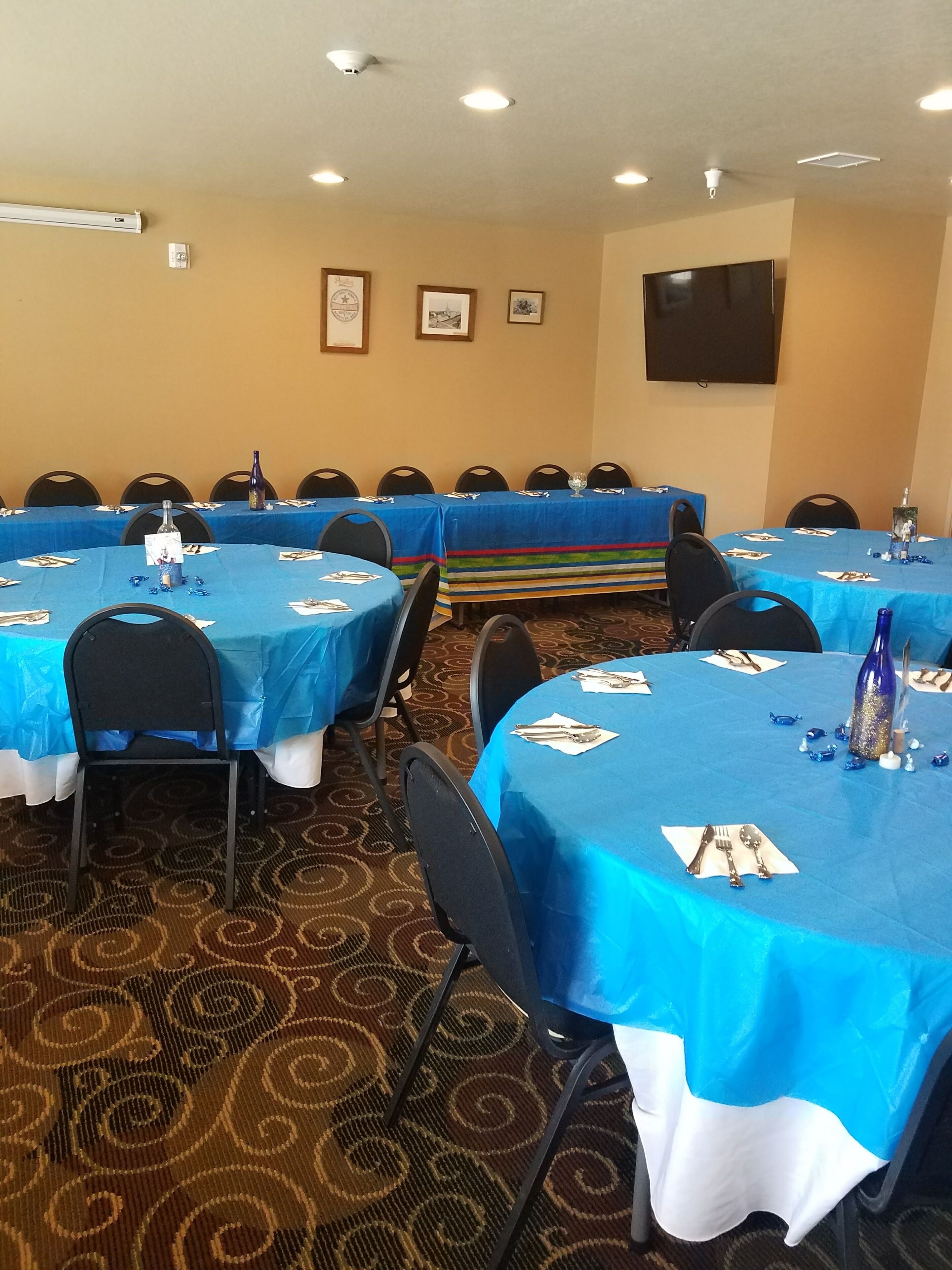 A conference room with multiple tables covered in blue tablecloths, equipped with chairs, and featuring a patterned carpet.