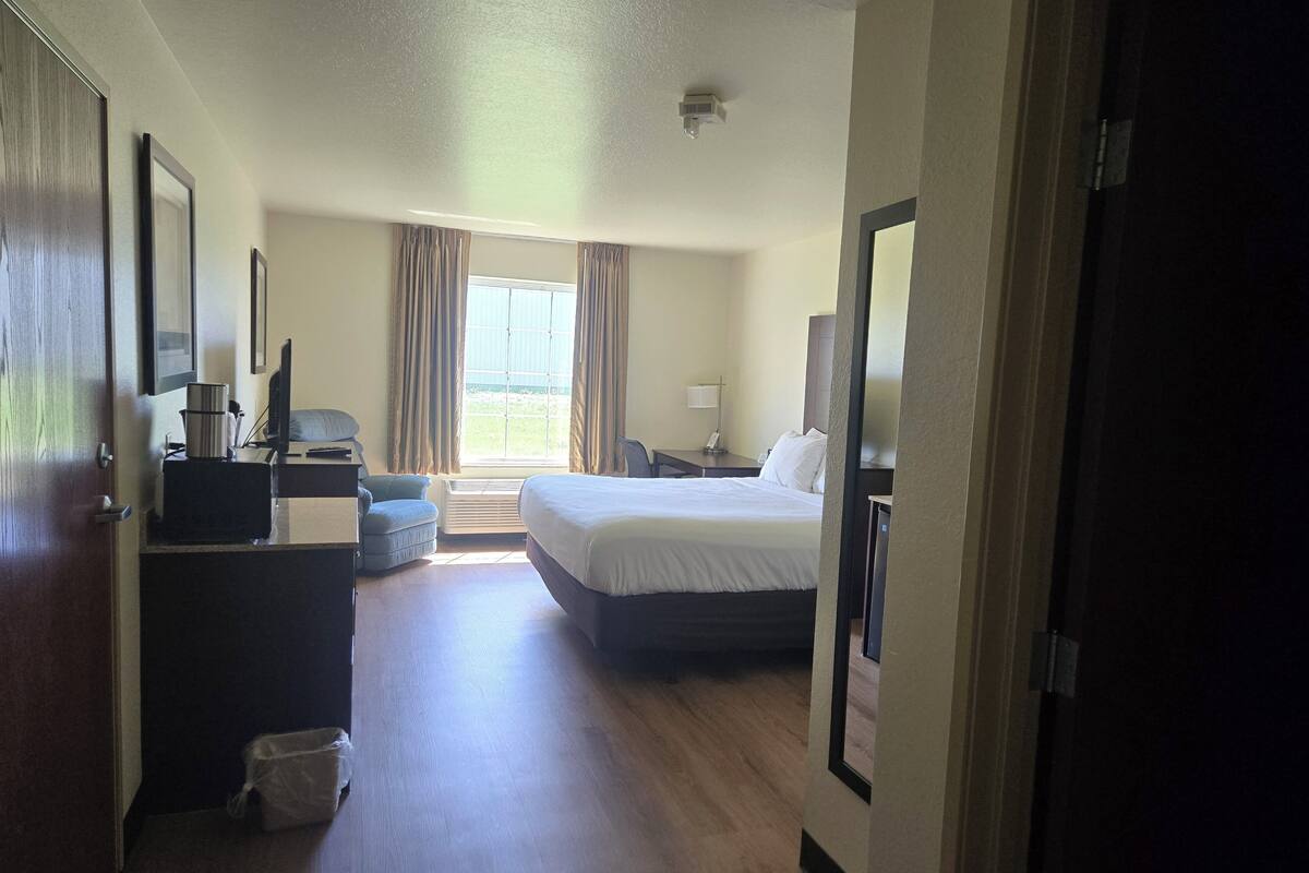 A hotel room with a bed, a desk with a computer, a chair, and a window with curtains.