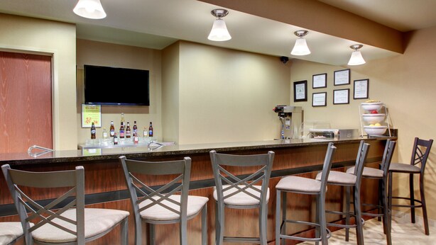 A bar area with a counter, multiple bar stools, a television mounted on the wall, and a variety of bottles on the counter.