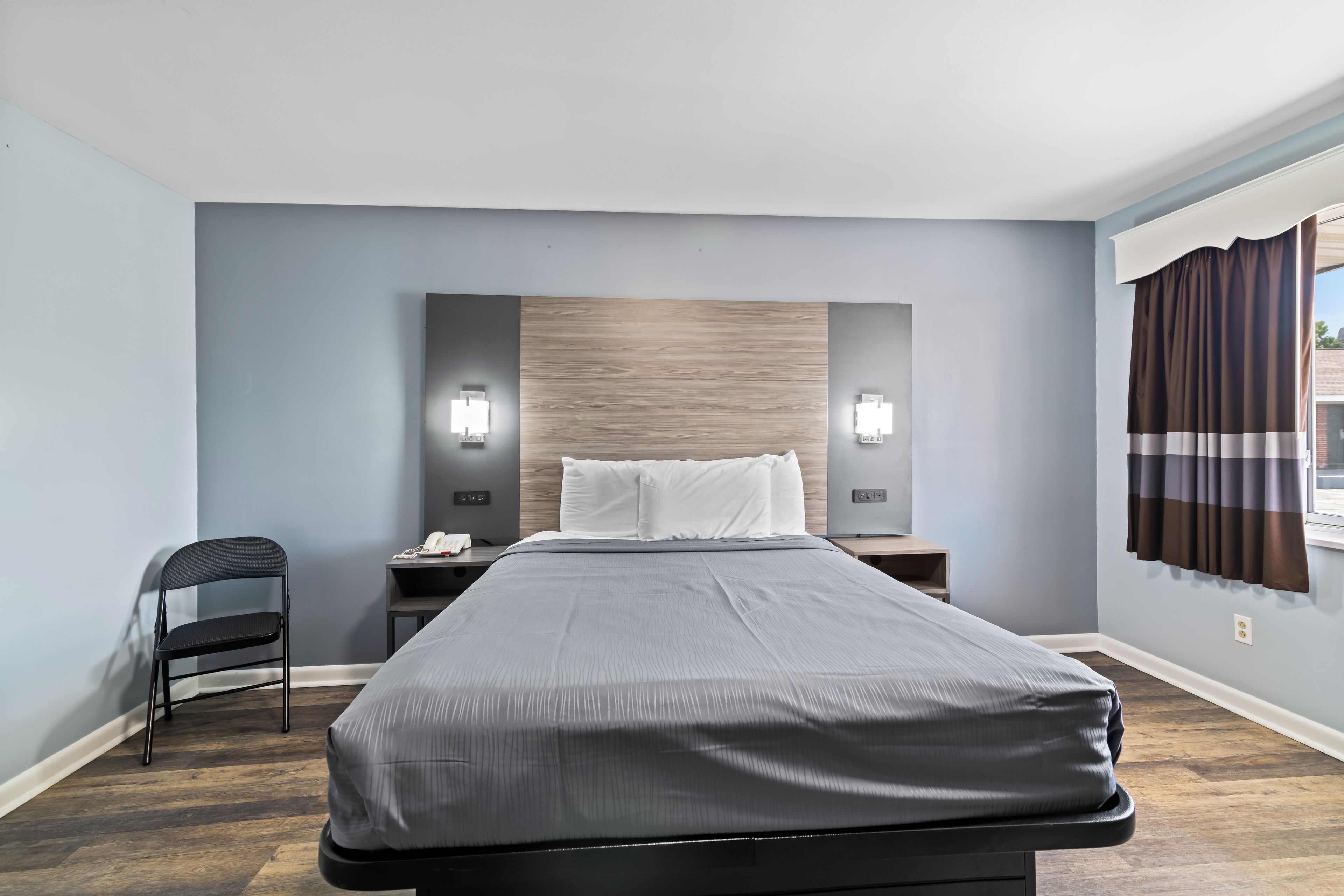 Ein modernes Hotelzimmer mit einem großen Bett, einem Sessel, einem Nachttisch und einem Fenster mit Vorhängen.