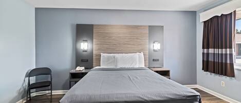 Una habitación de hotel moderna con una cama grande, una silla, una mesita de noche y una ventana con cortinas.