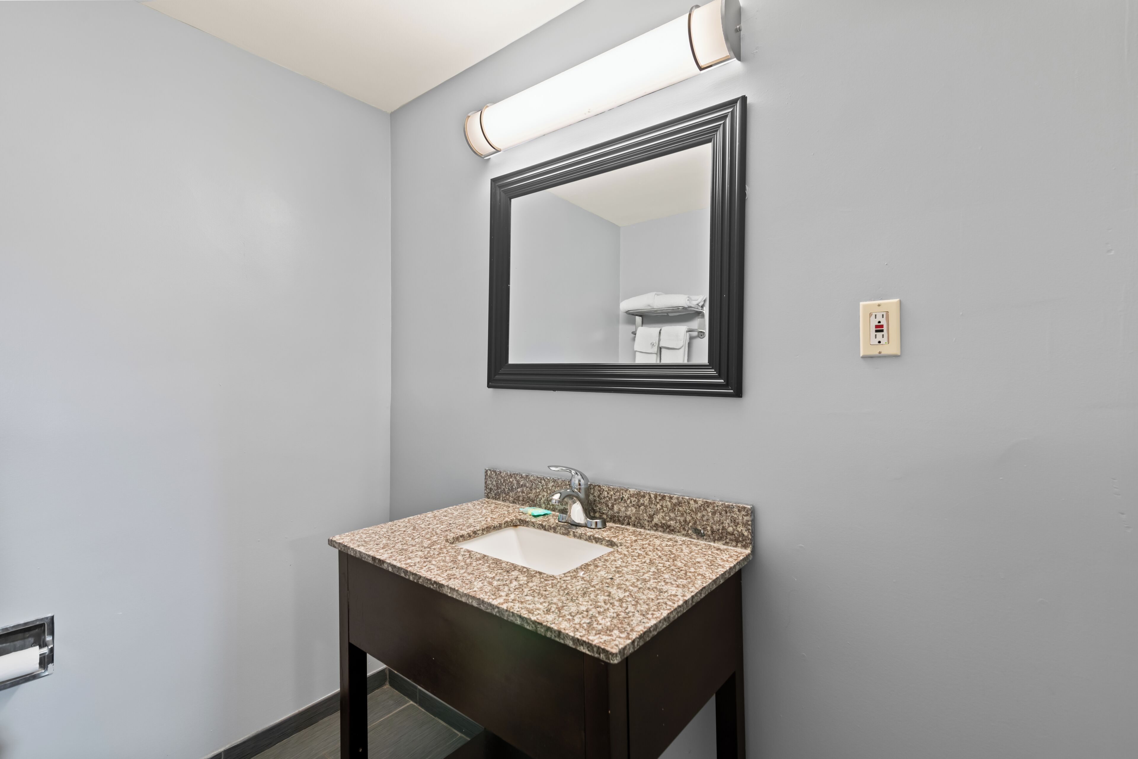 A bathroom with a granite countertop sink, a mirror, and a towel rack.
