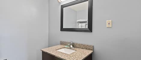 A bathroom with a granite countertop sink, a mirror, and a towel rack.