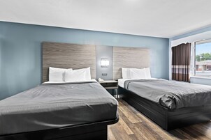Habitación de hotel con dos camas, una mesita de noche, una lámpara de pared y una ventana con cortinas.