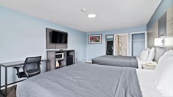 A hotel room with two beds, a desk, a chair, a TV, and a bathroom visible through an open door.