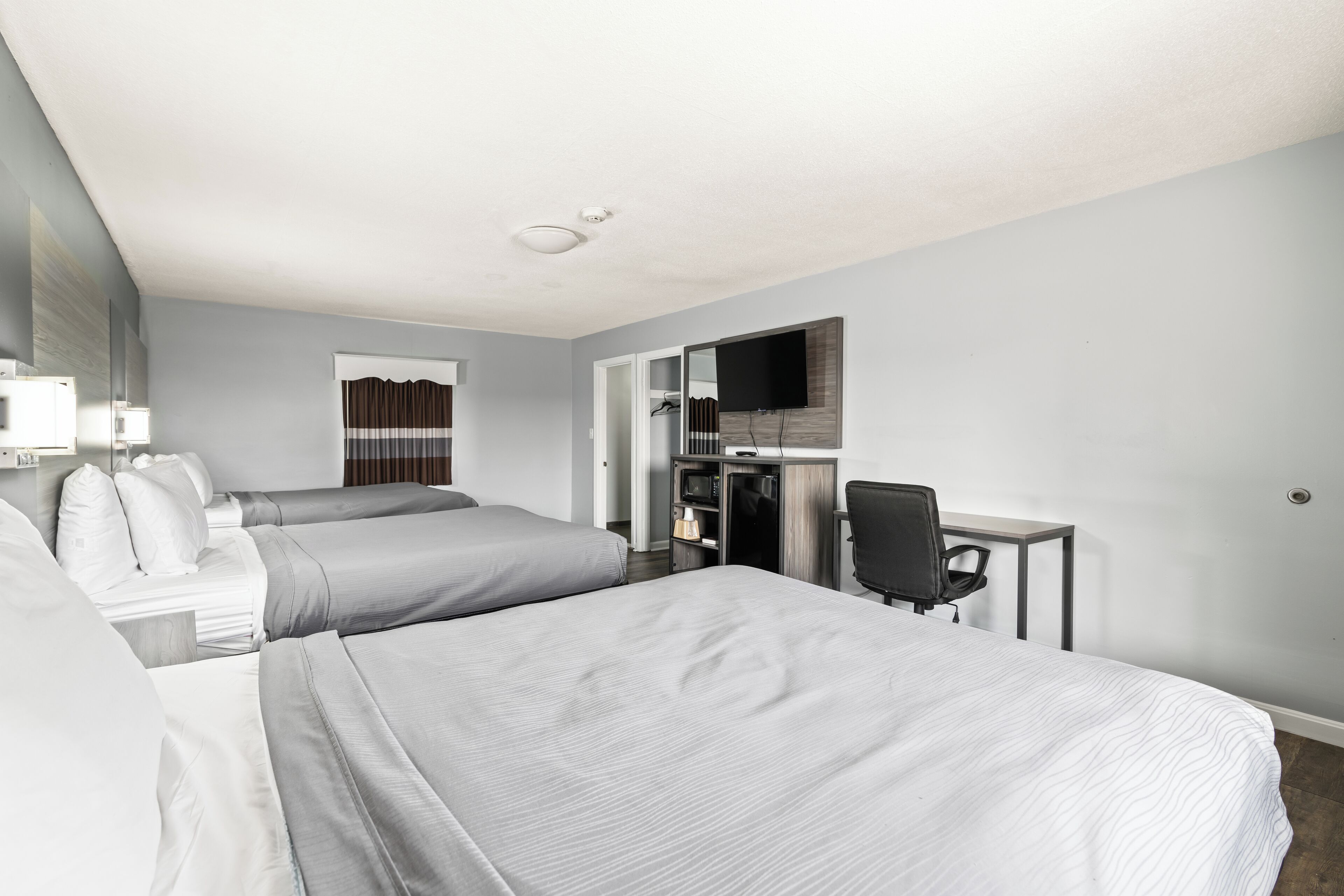 A hotel room with two beds, a desk, a chair, a TV, and a wardrobe.