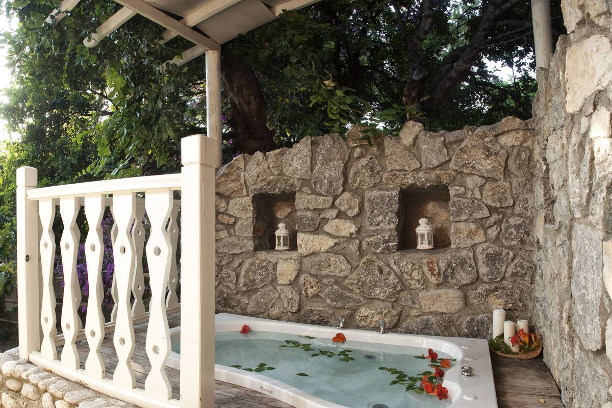 Un muro de piedra con dos faroles, una terraza de madera y un jacuzzi con flores.