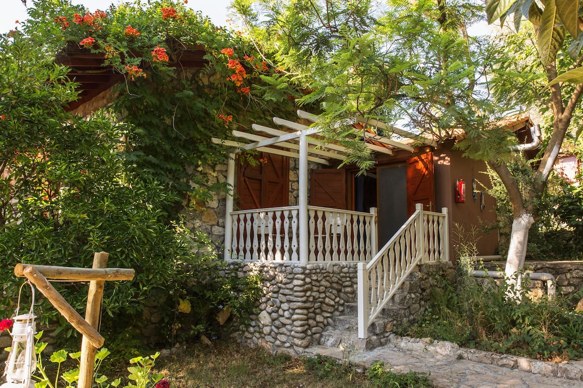 Un edificio de paredes de piedra con una pérgola de madera y una escalera que lleva a una puerta de madera.