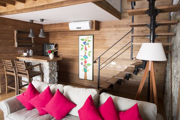 A cozy living area with a sofa, bright red cushions, a wooden staircase, and a kitchen area with bar stools and a refrigerator. - Nautical Hotel Adults Only (Fethiye)