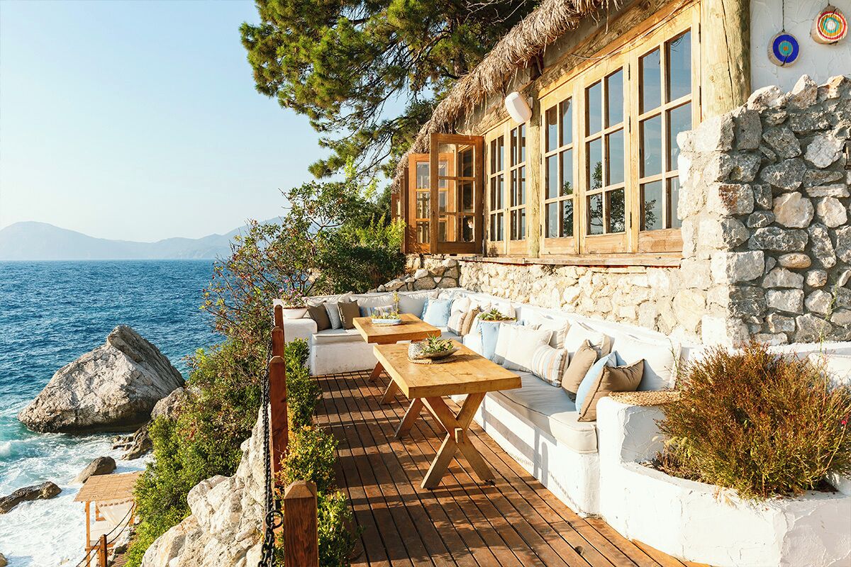 A coastal property with a stone exterior, wooden deck, and outdoor seating area overlooking the sea.