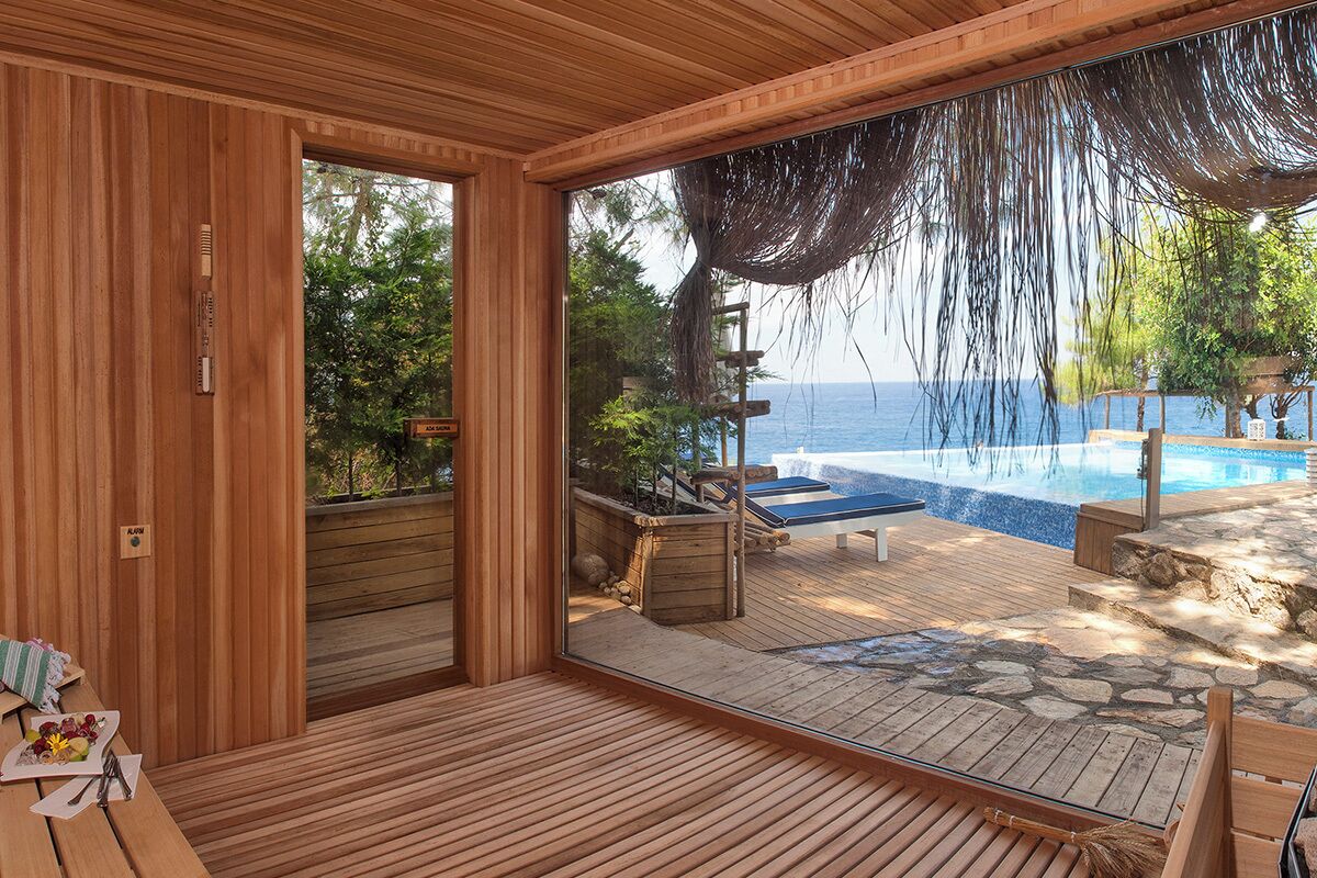 A wooden deck with a stone pathway leading to a pool, a wooden bench, and a view of the sea.