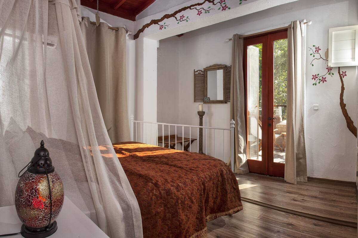 Un dormitorio con cama, mesita de noche, lámpara y ventana con cortinas.