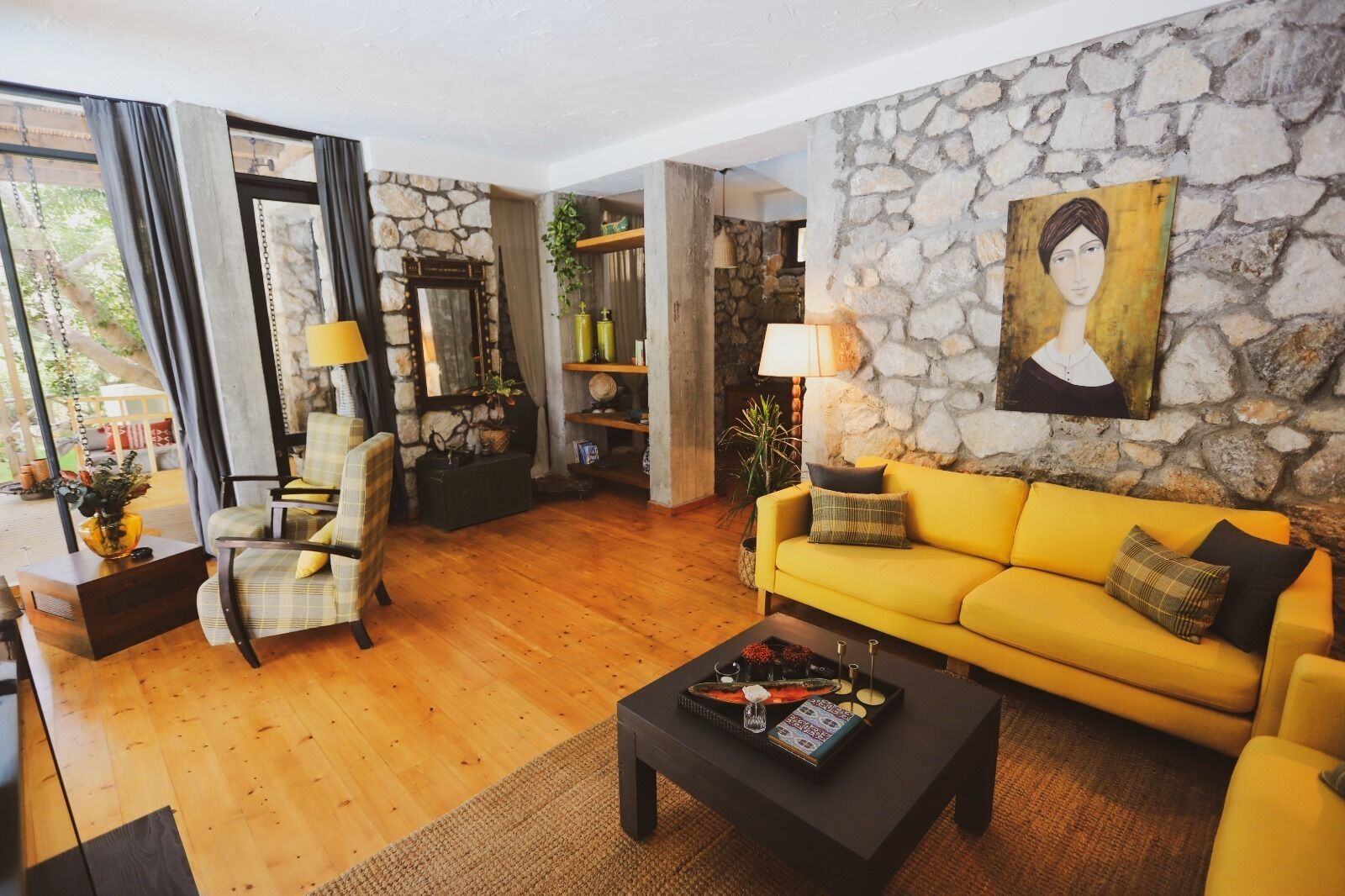 Una sala de estar con un sofá amarillo, un sillón escocés y una mesa de centro. Se ve una pared de piedra y un cuadro.