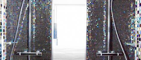 A bathroom with two showerheads and a tiled mosaic wall.