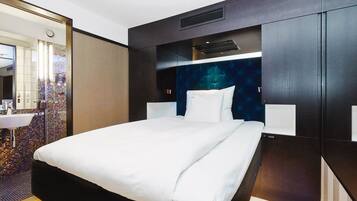 Una habitación de hotel moderna con una cama grande, un escritorio integrado y un baño con un vibrante mosaico en el fondo.