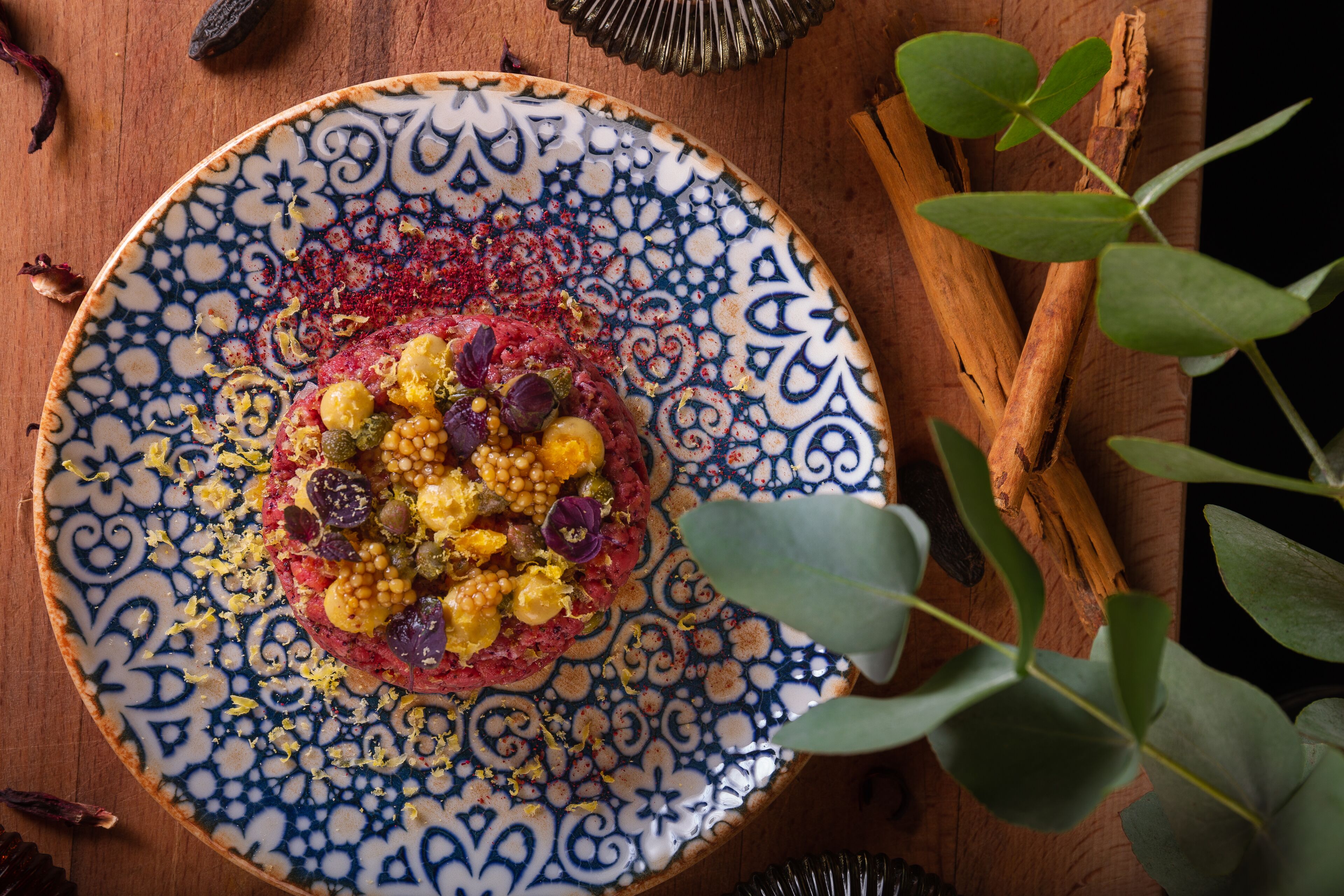 A plate with a colorful dish, surrounded by eucalyptus leaves and cinnamon sticks on a wooden surface.