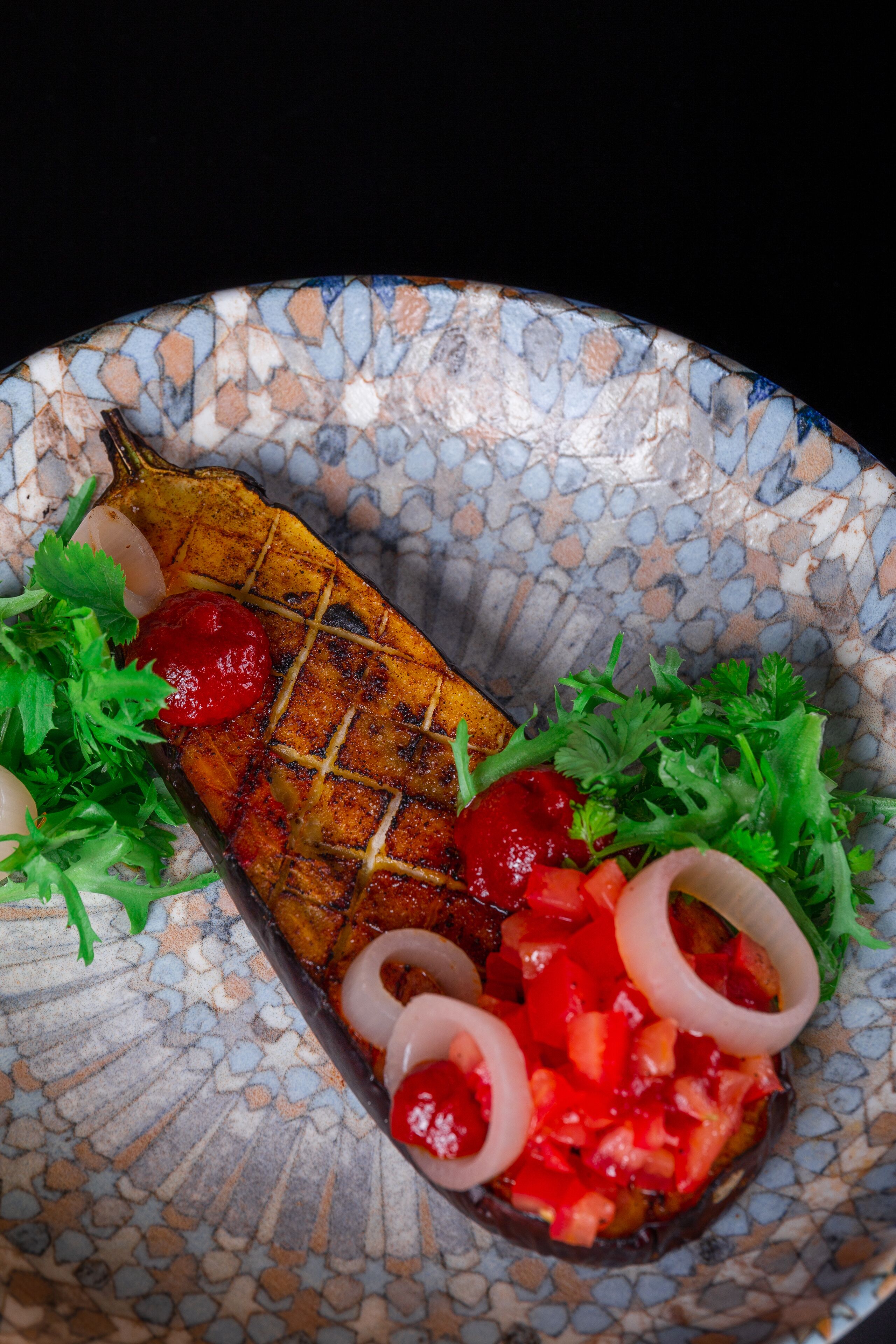 A plate with grilled fish, red peppers, onions, and herbs.