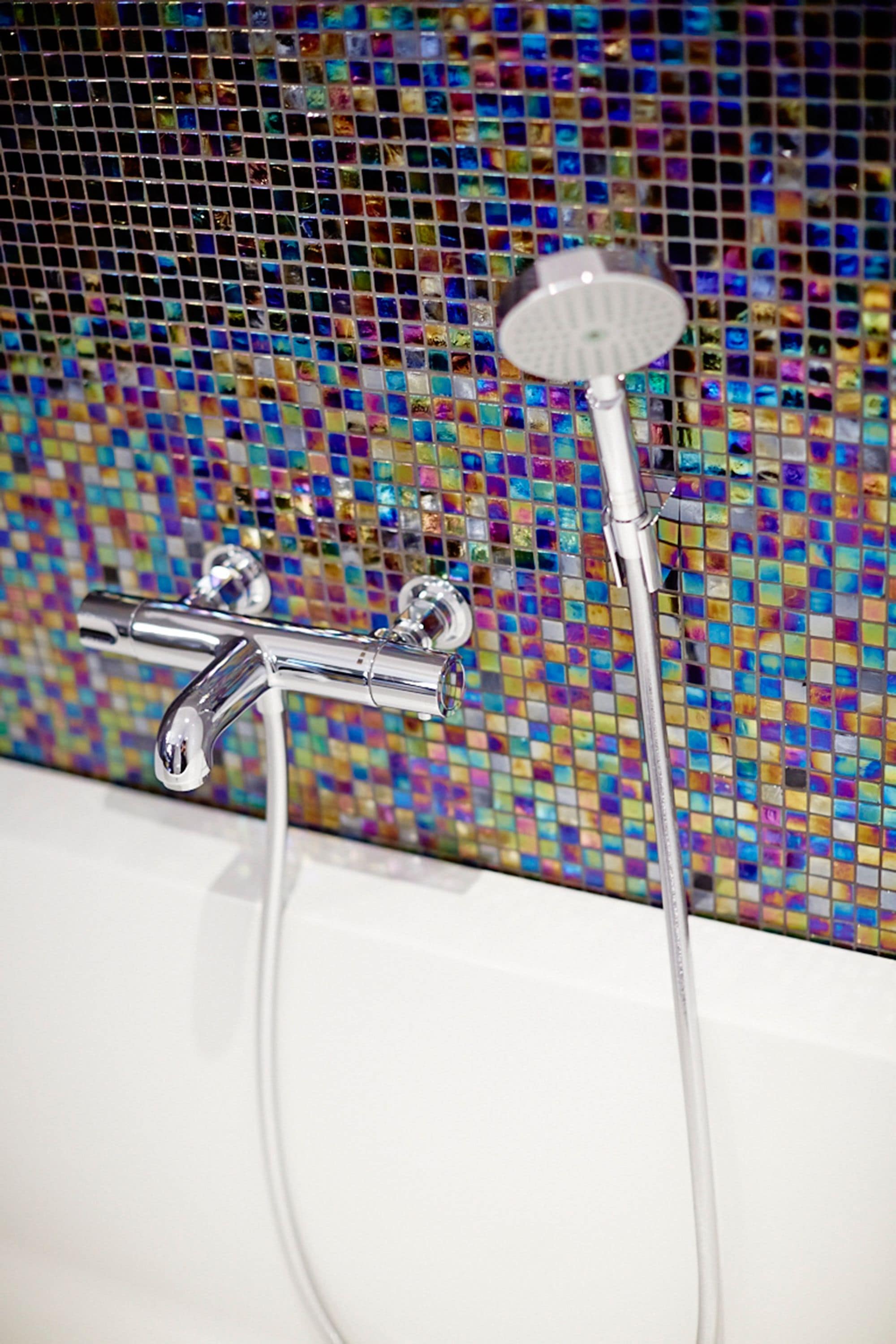 A bathroom with a shower head and faucet against a mosaic tile wall.