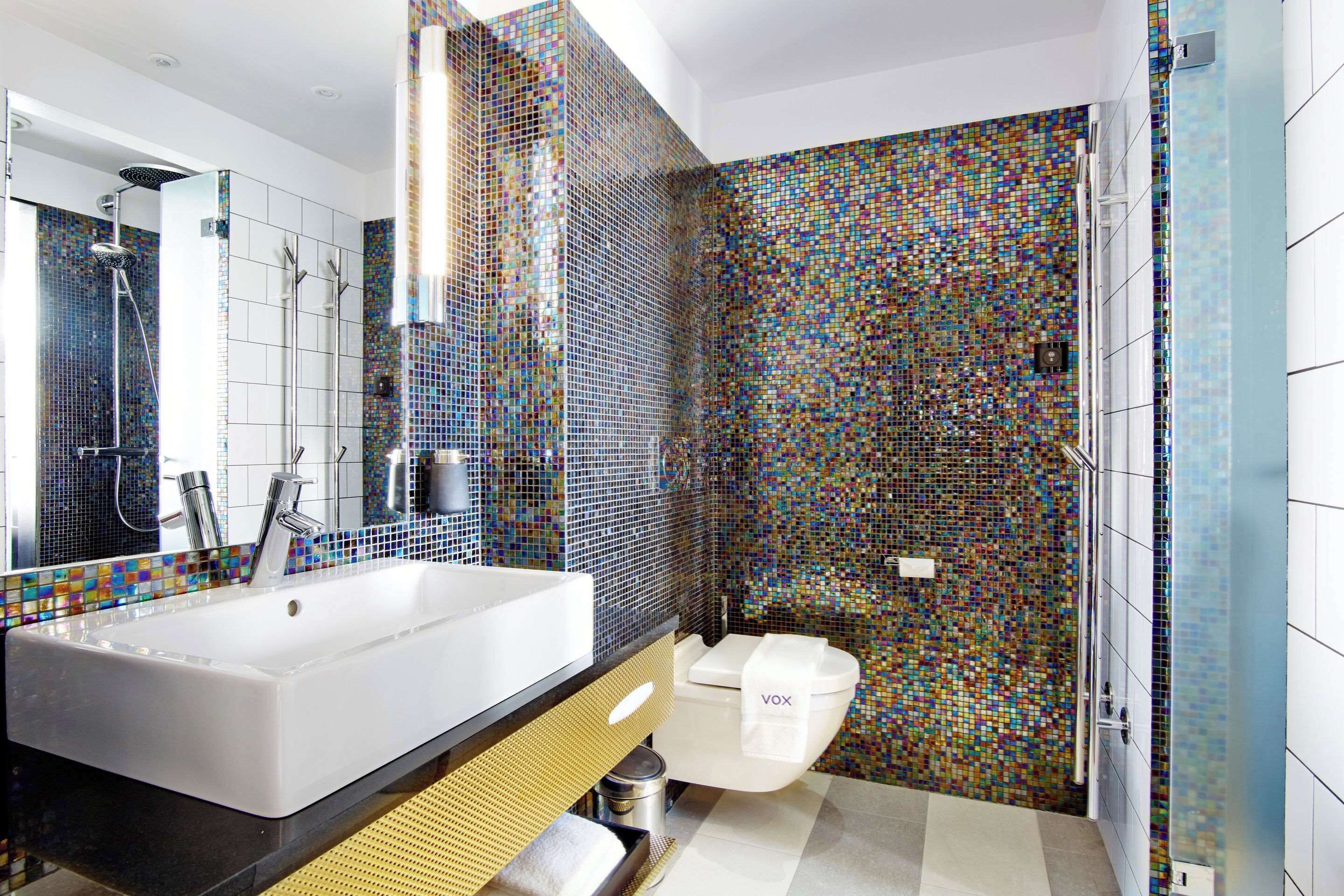 A modern bathroom with a large white bathtub, a gold vanity, and a mosaic tile wall.