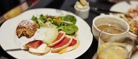 Una mesa de comedor con platos de comida, incluyendo un croissant, fruta y una ensalada.