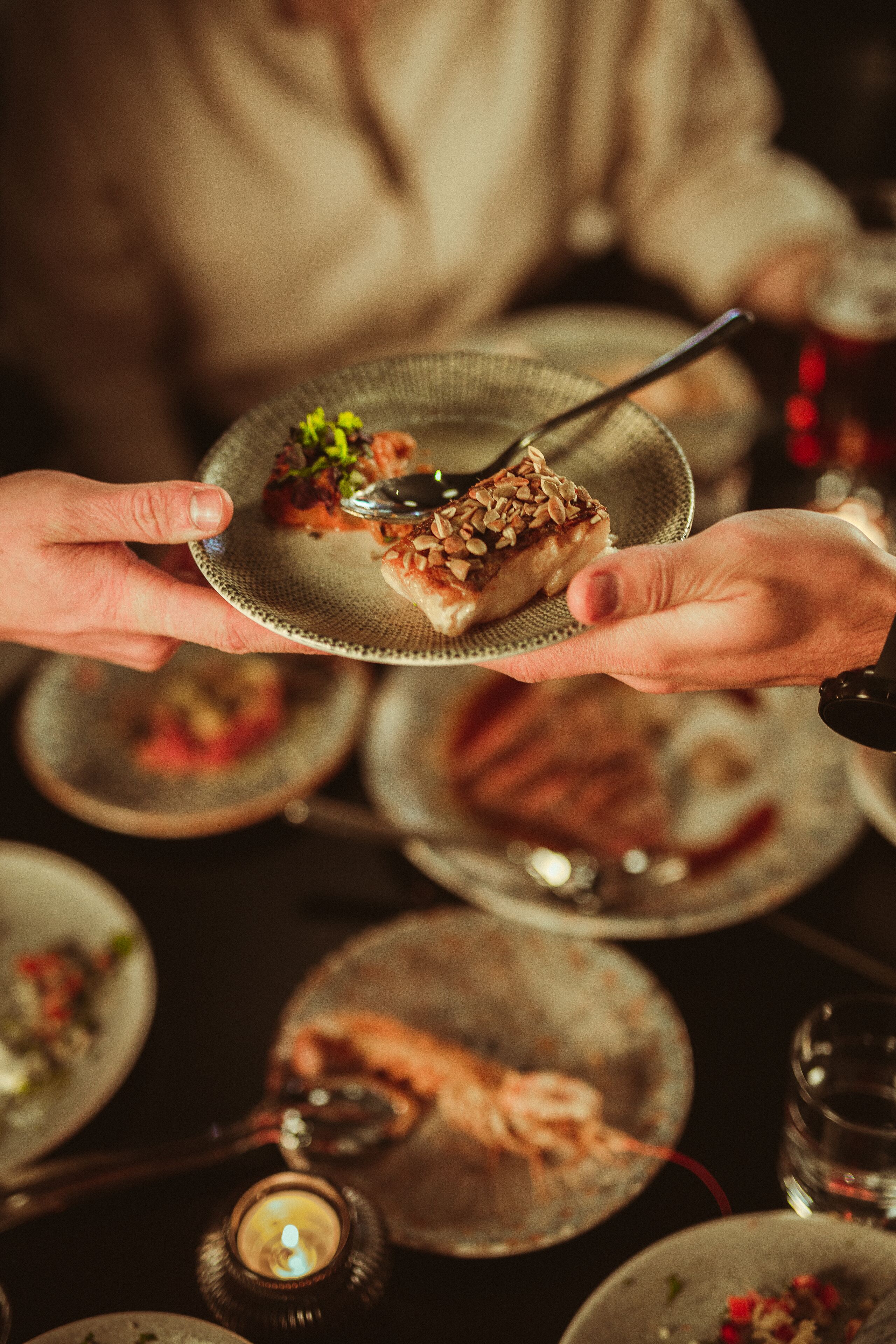 A person holding a plate with a dessert, surrounded by other plates and a candle.