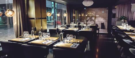 A restaurant with tables set for dining, large windows, and hanging pendant lights.