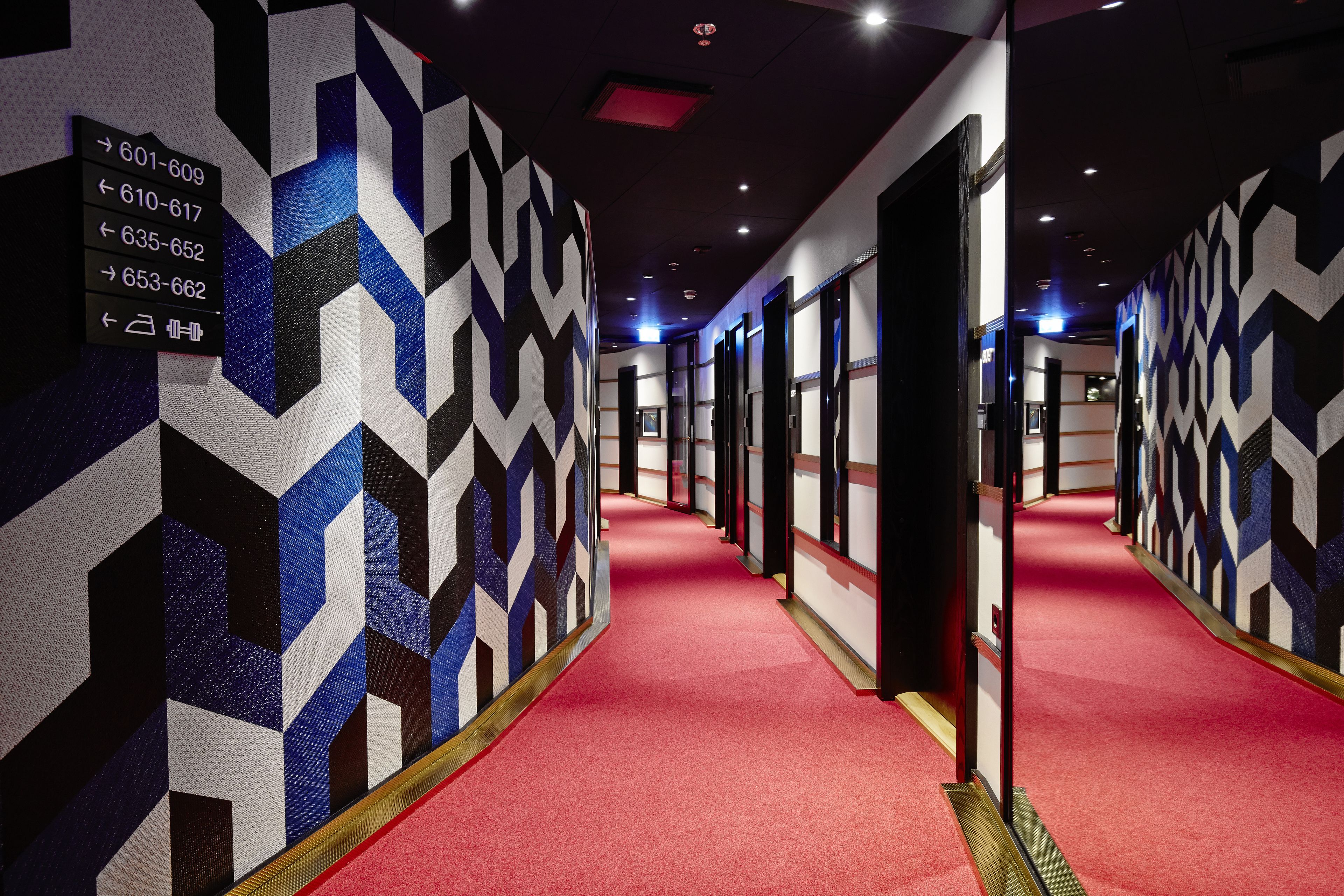 Un pasillo de hotel con paredes de diseño geométrico y alfombra roja.