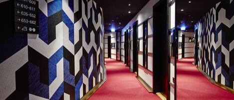 A hotel hallway with geometric patterned walls and a red carpet.