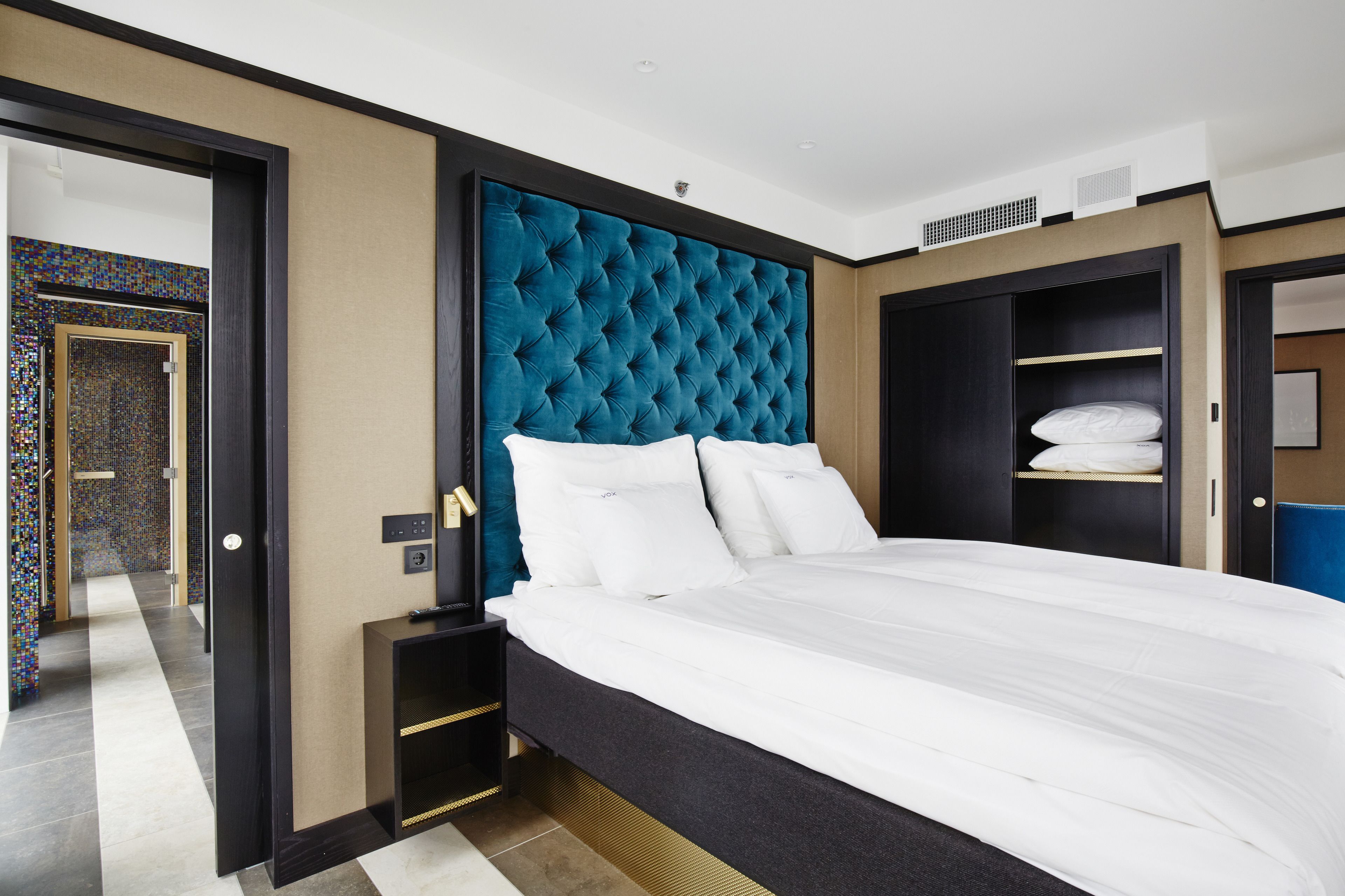 A modern hotel room with a large bed, a dark headboard, and a walk-in closet.