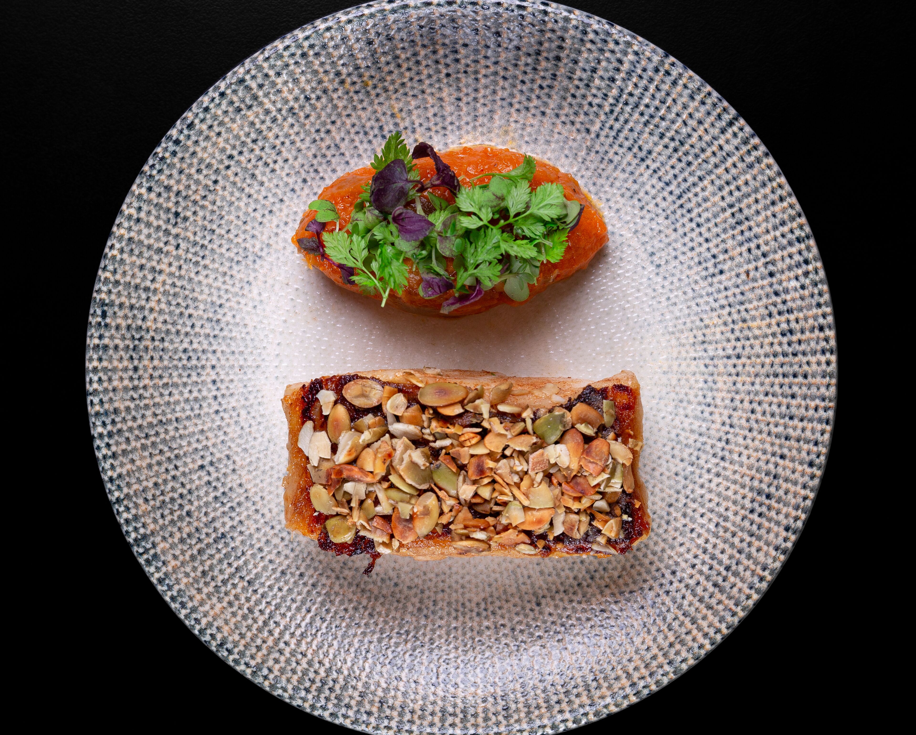 Un plato con una rebanada de pan cubierta de nueces y un trozo de salmón con hierbas.
