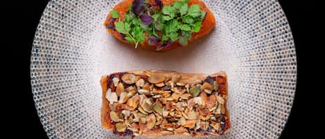 Un plato con una rebanada de pan cubierta de nueces y un trozo de salmón con hierbas.