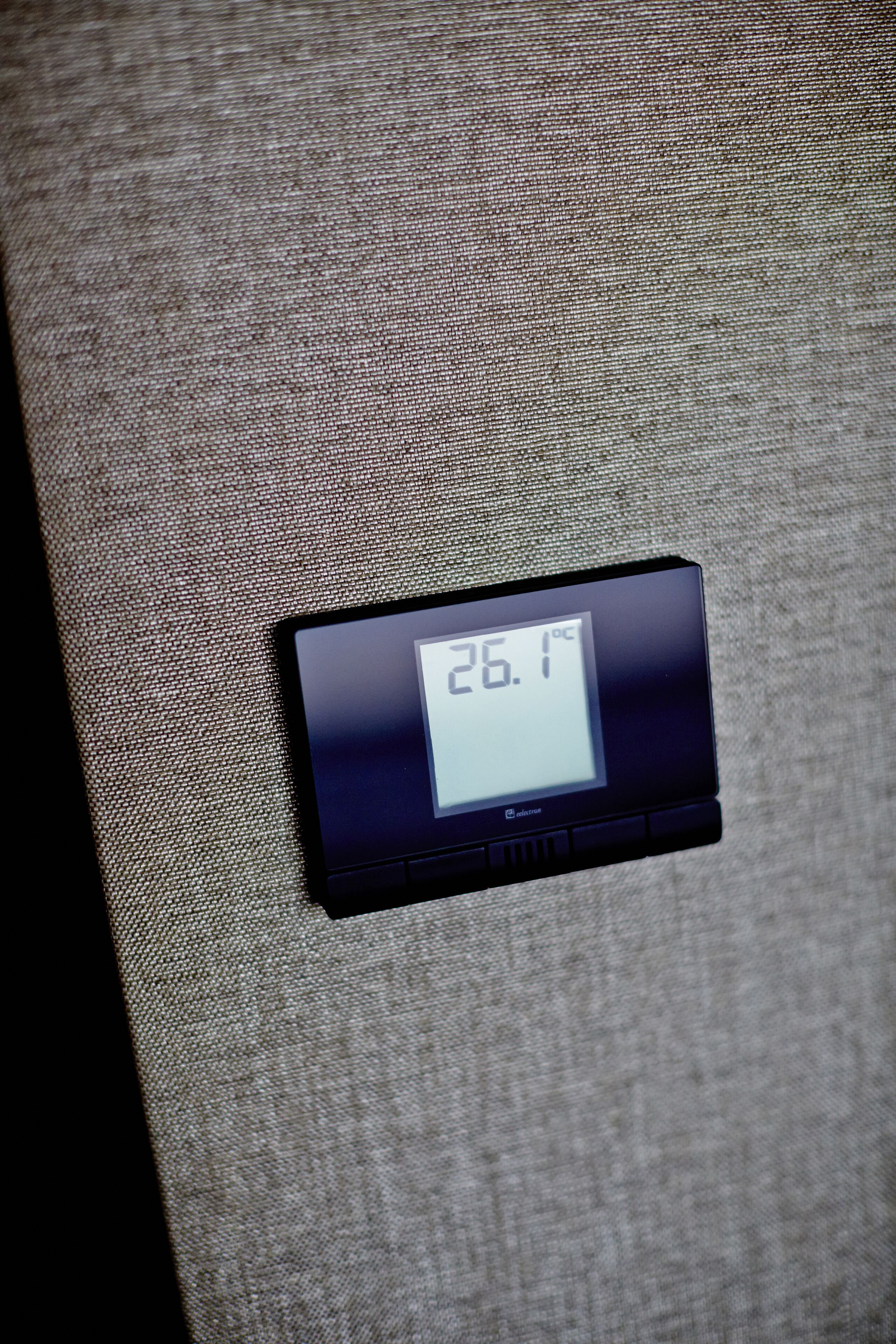 Termostato digital mostrando uma temperatura de 26,1°C sobre uma superfície de tecido texturizado.
